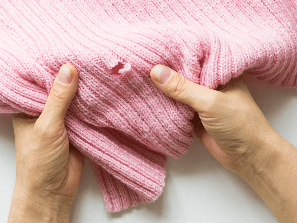 Person holding a pink sweater and showing a fish moth hole.