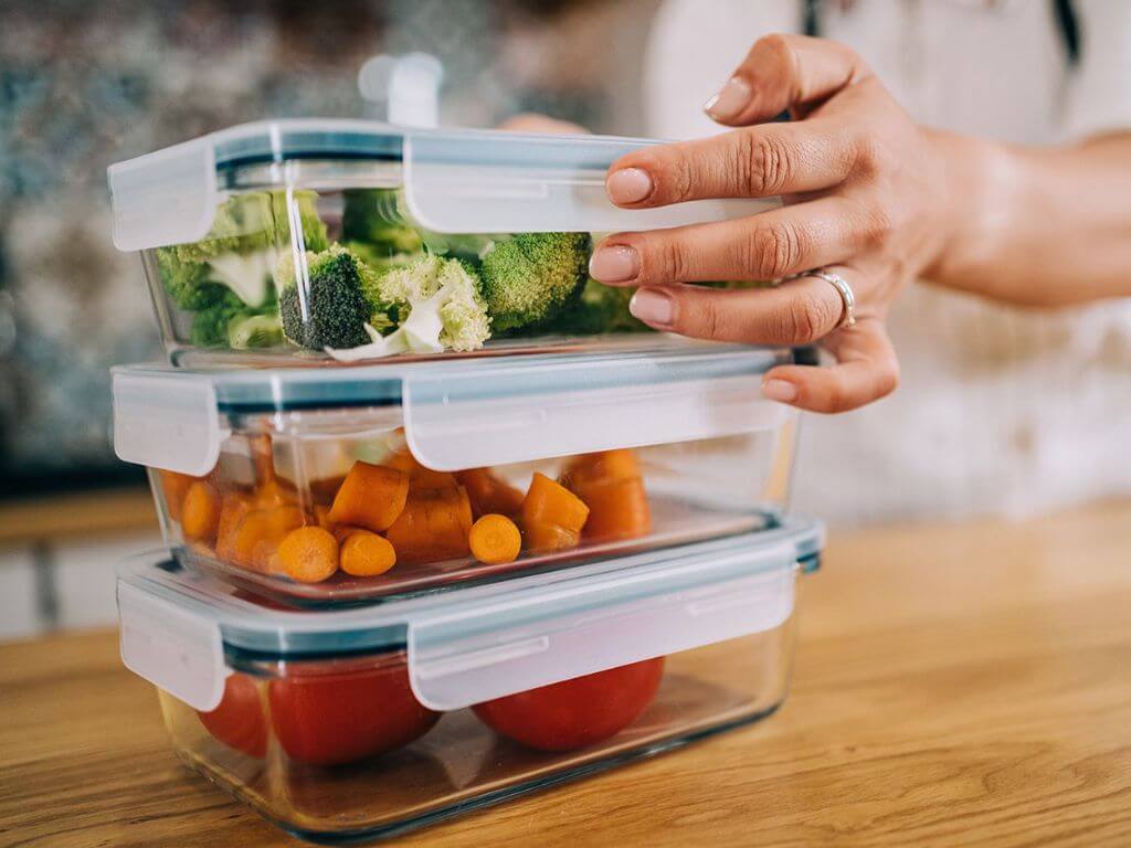 A person’s hand placing airtight containers of chopped vegetables on a wooden table.
